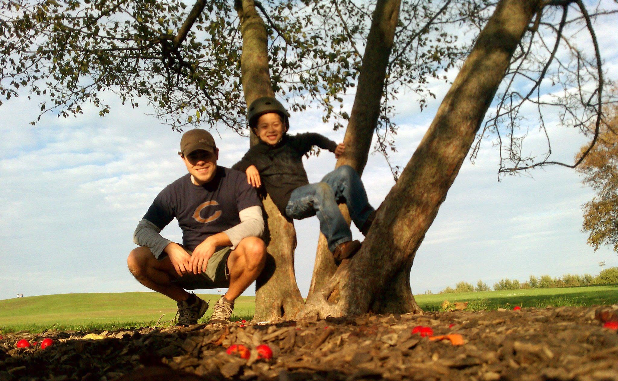 A father and son together outdoors in a Chicago park, climbing and posing by a tree